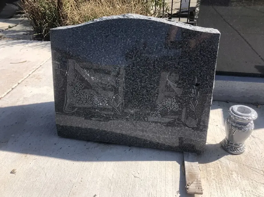 Grey granite slant headstone with a carved floral scroll panel