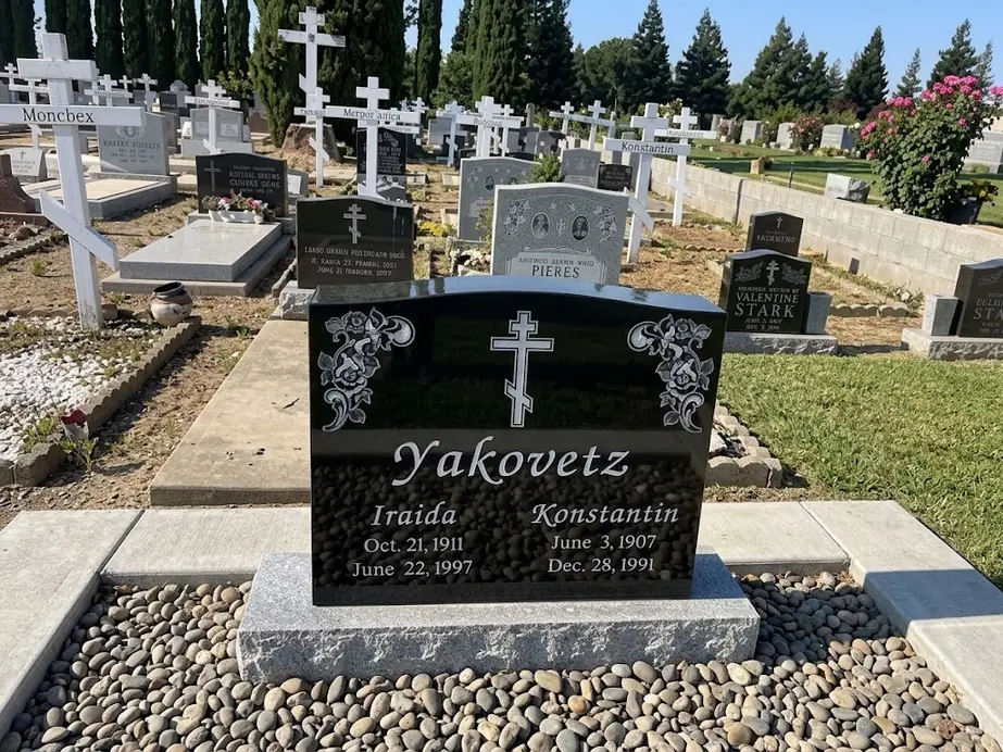 Black granite double headstone with an Orthodox cross and etched roses on a pebble bed